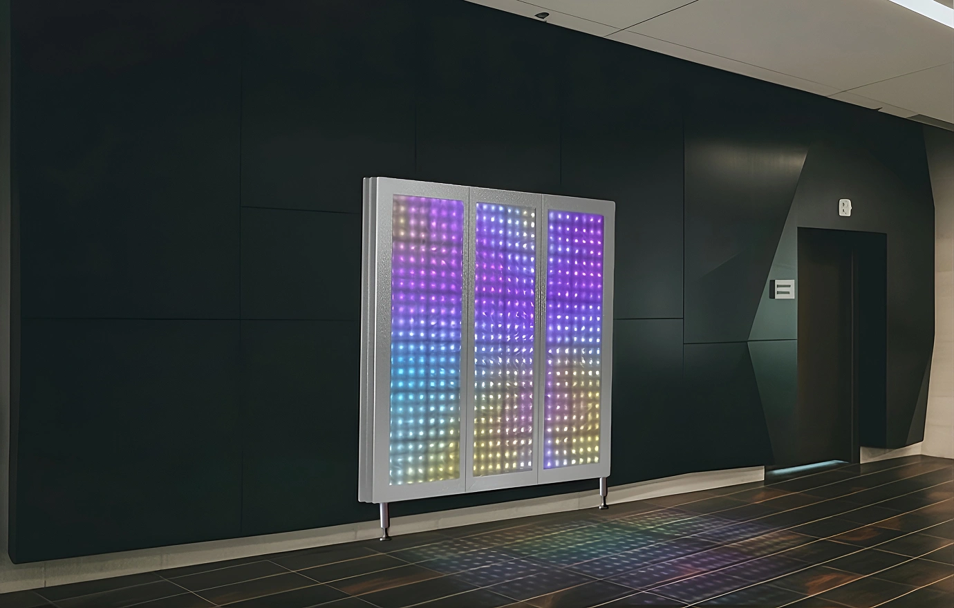 Colorful LED light panel mounted on a dark wall beside an elevator, with light reflections on the tiled floor